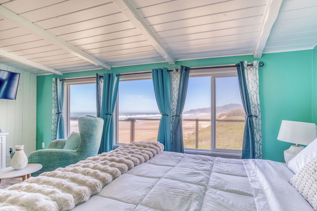 A bedroom with a bed, a chair, a TV, and a window with curtains.