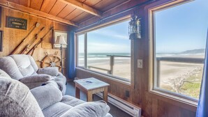 Une pièce chaleureuse avec un plafond en bois, une grande fenêtre donnant sur la plage, une petite table et un canapé.