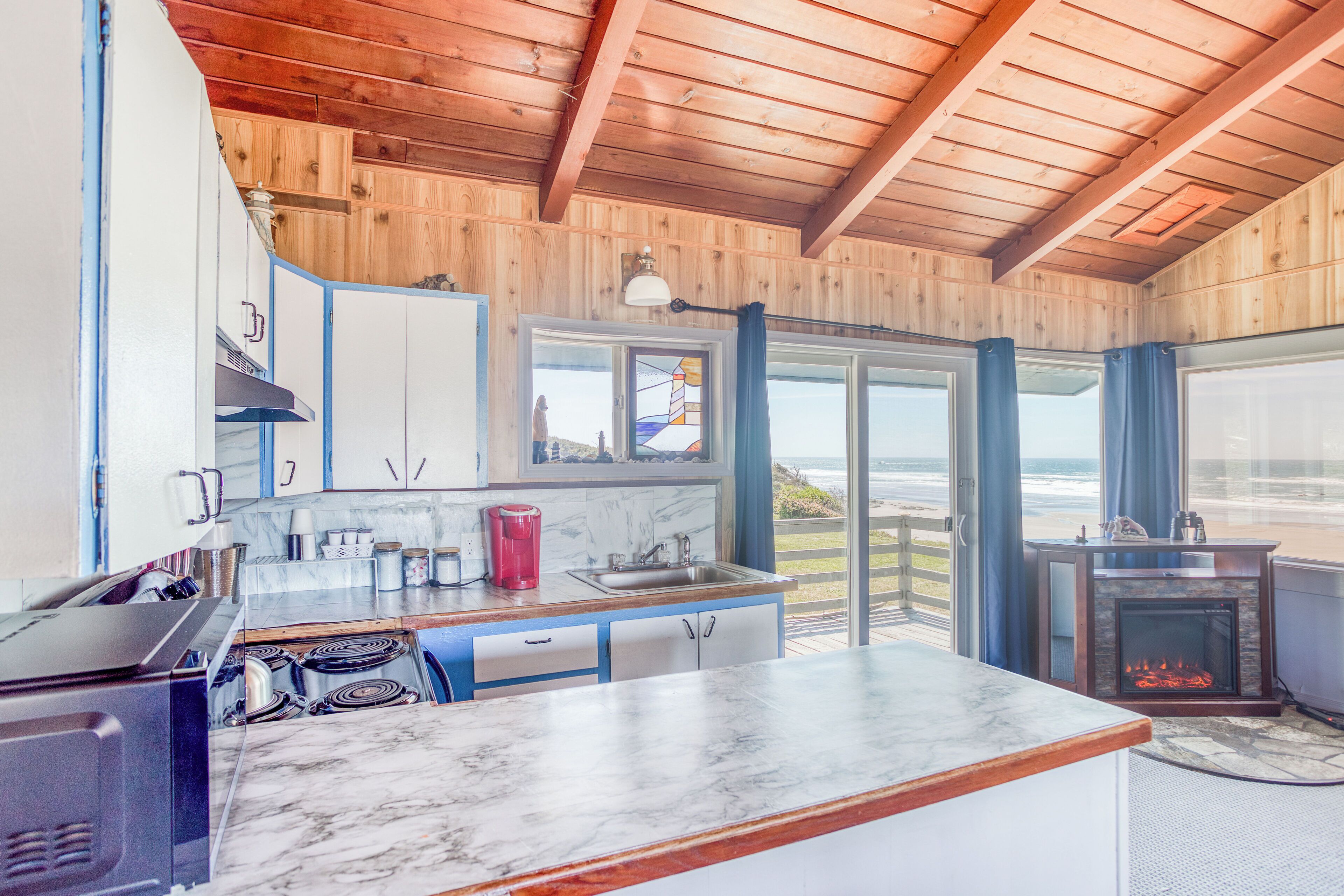 A kitchen with a marble countertop, wooden ceiling, and a view of the ocean through large windows.