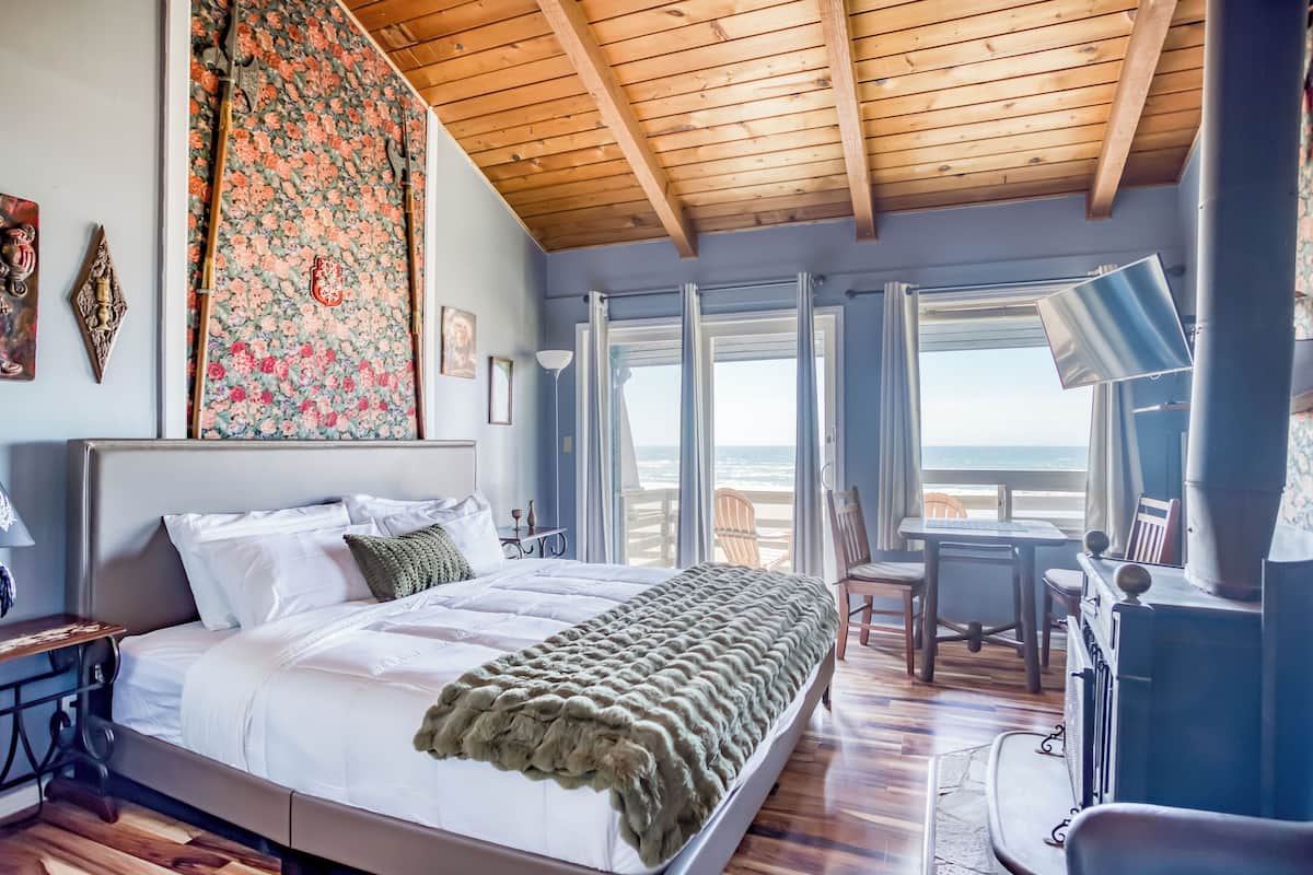 A bedroom with a large bed, wooden ceiling, and a view of the beach.