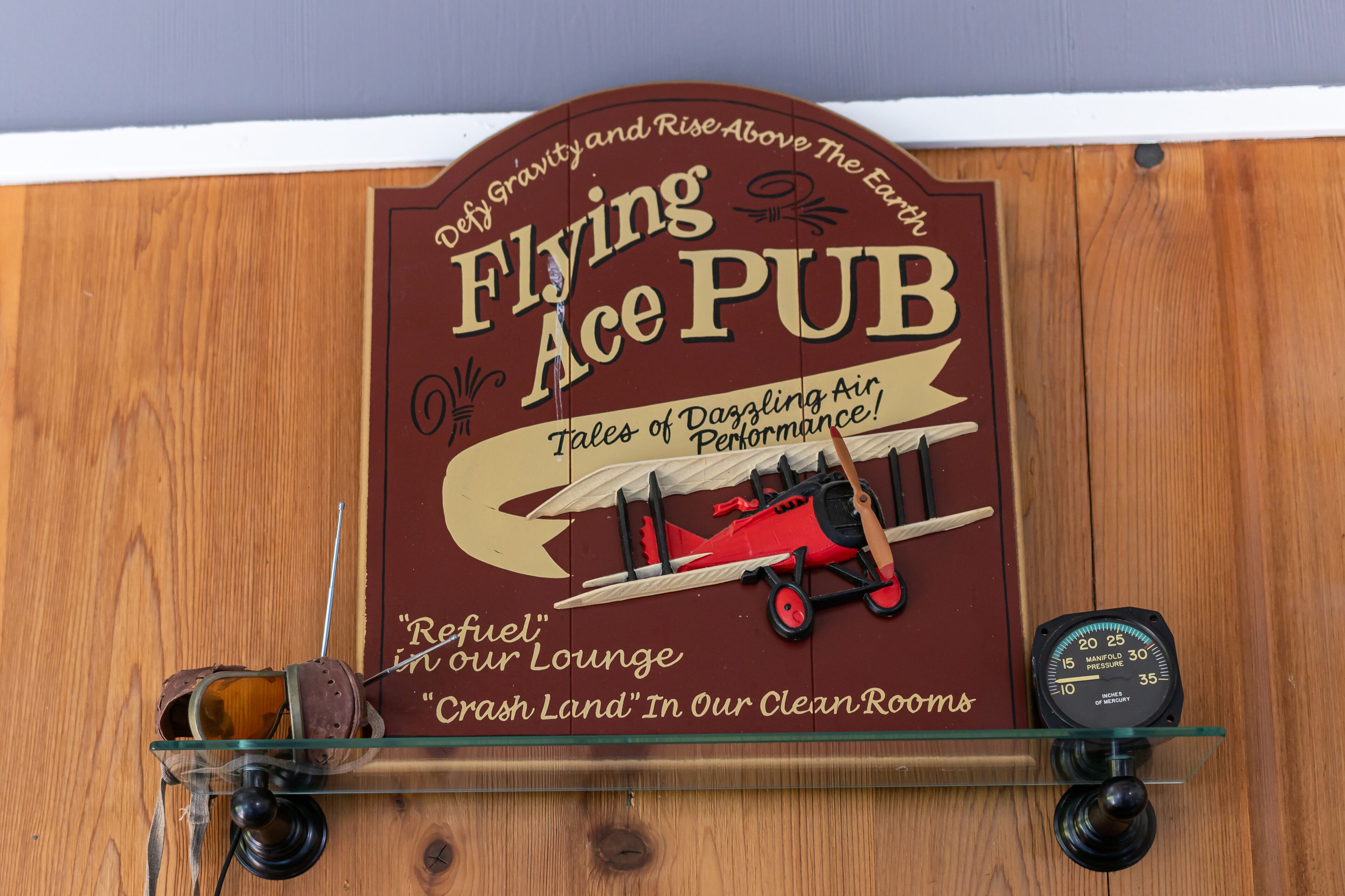 A wooden wall with a sign for 'Flying Ace Pub' featuring a red biplane and a pressure gauge.