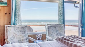 Une chambre avec vue sur la plage, un lit agrémenté d’oreillers à motifs floraux, une petite table avec deux verres et une porte bleue.