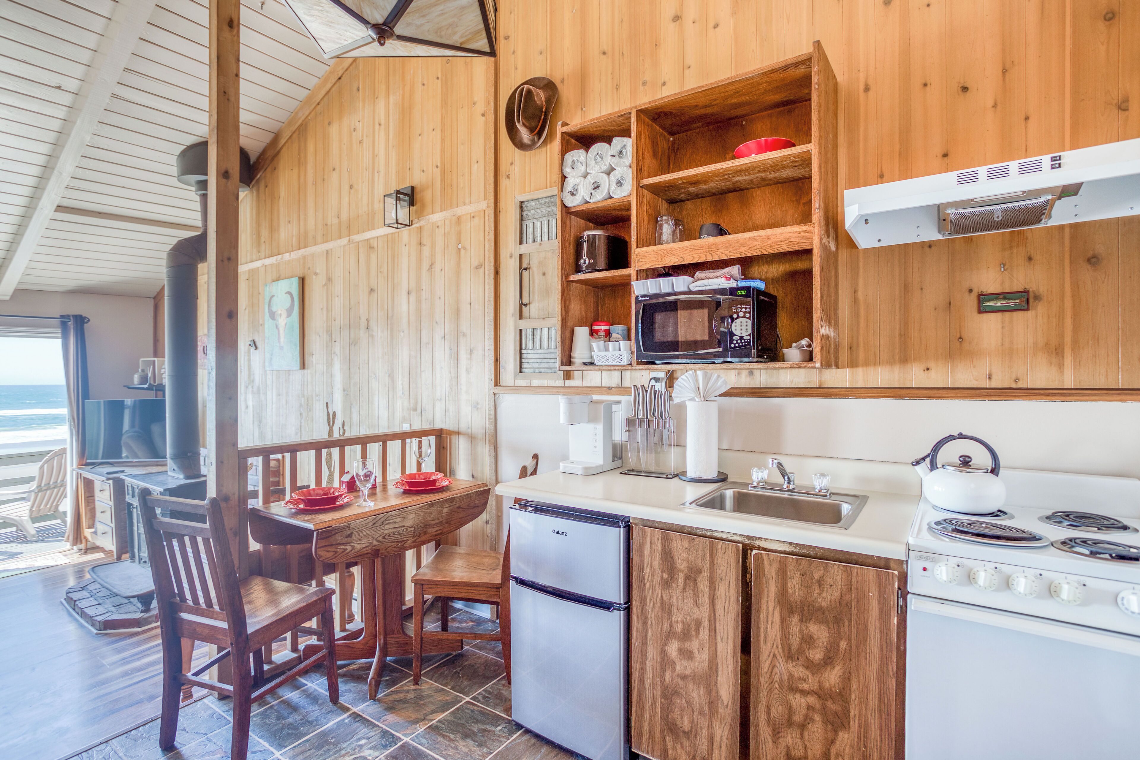 A wooden kitchen with a refrigerator, stove, microwave, and wooden shelves.