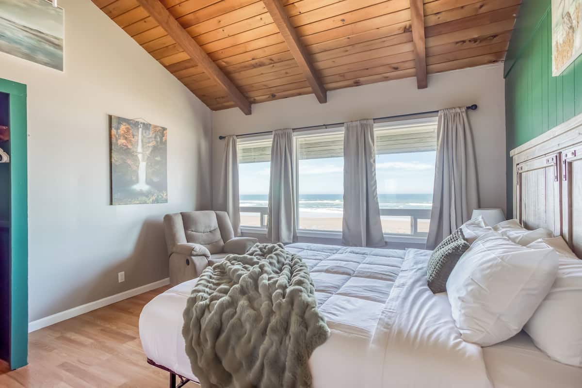 A bedroom with a large bed, a chair, and a view of the beach.