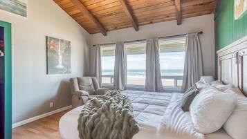 Un dormitorio con una cama grande, una silla y vistas a la playa.