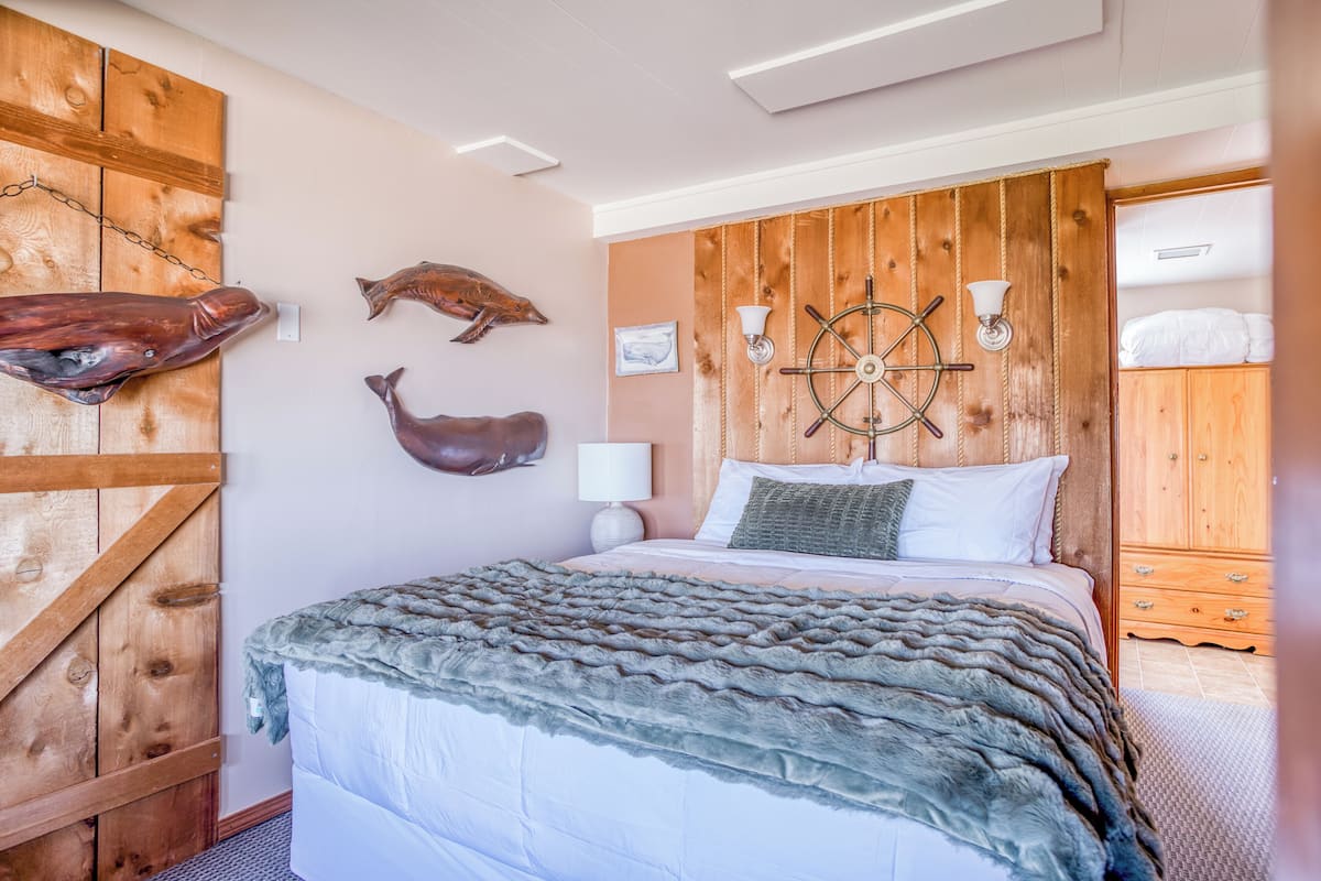 A bedroom with a wooden headboard, a bed with white bedding, a fur throw, and a ship's wheel decoration.