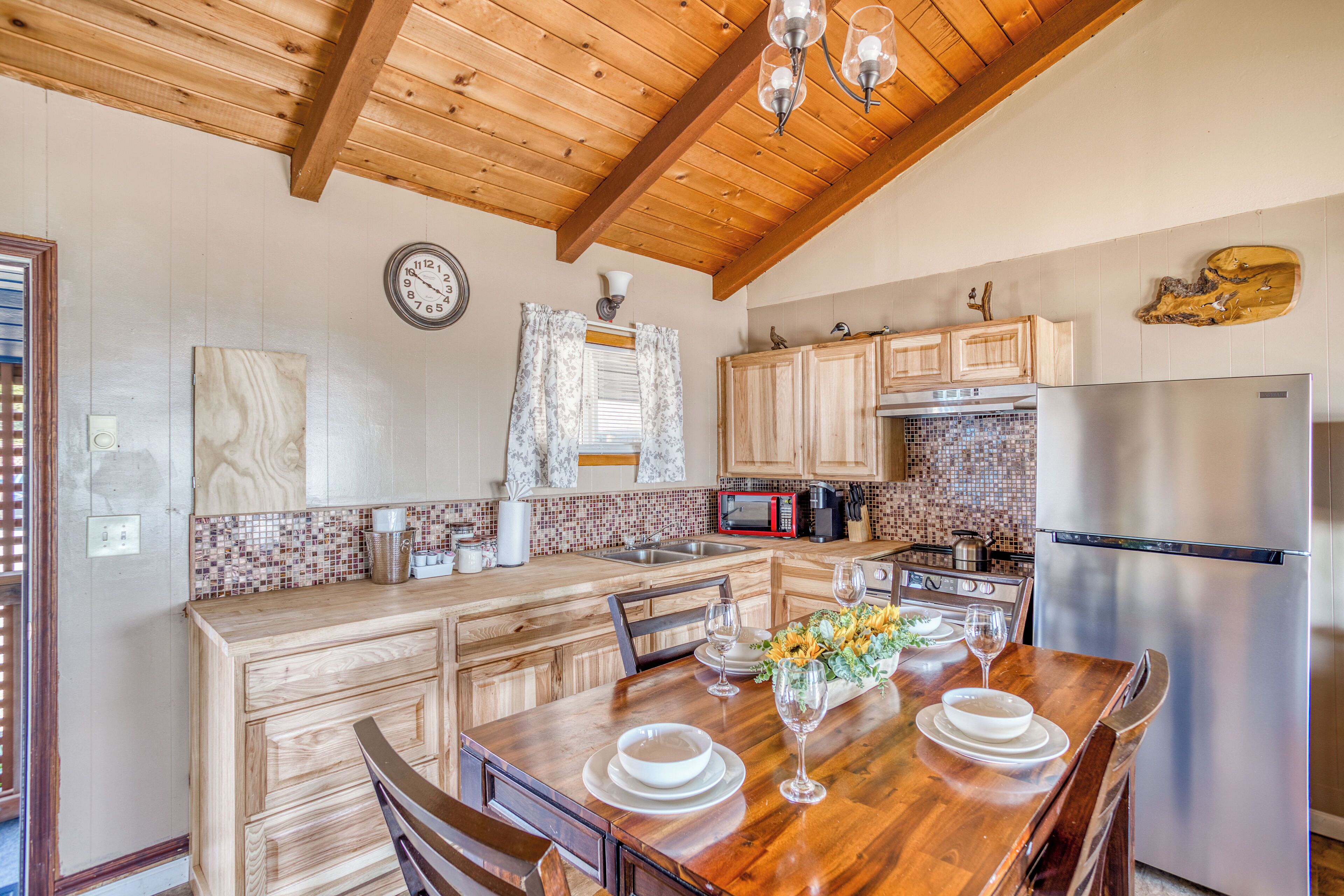 A kitchen with wooden cabinets, a stainless steel refrigerator, and a dining table set with plates and glasses.