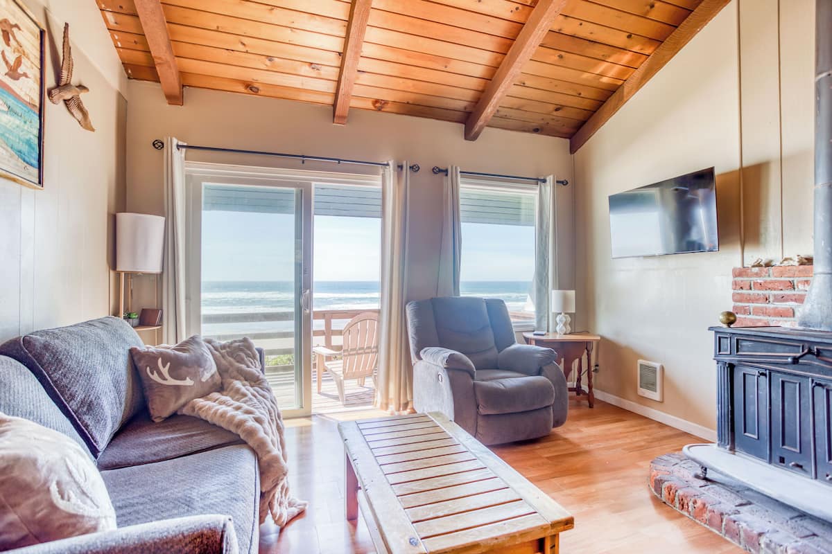 A cozy living room with a wooden ceiling, a sofa, a chair, and a fireplace.