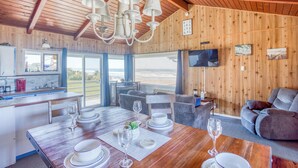 Un intérieur en bois comprenant un coin repas, une cuisine et un espace salon, avec de grandes fenêtres et un téléviseur.
