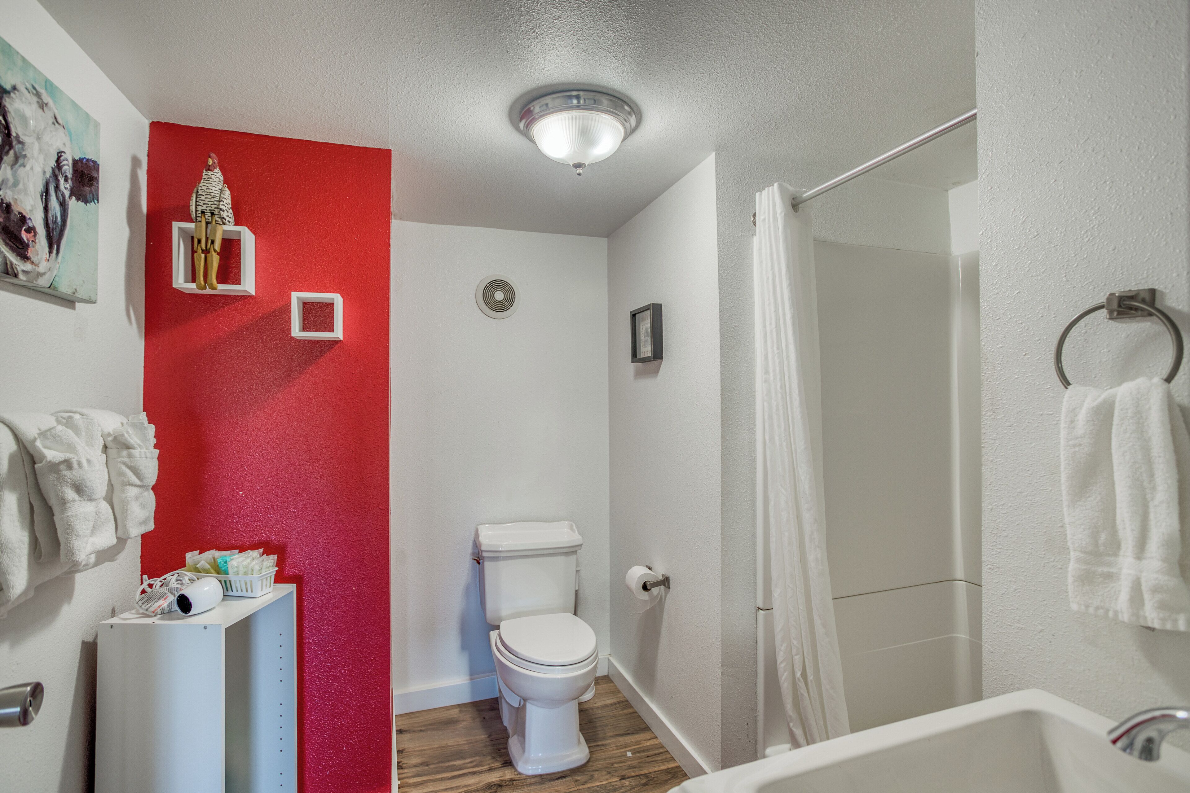 A bathroom with a white toilet, a shower with a glass door, a white sink, and a red accent wall.