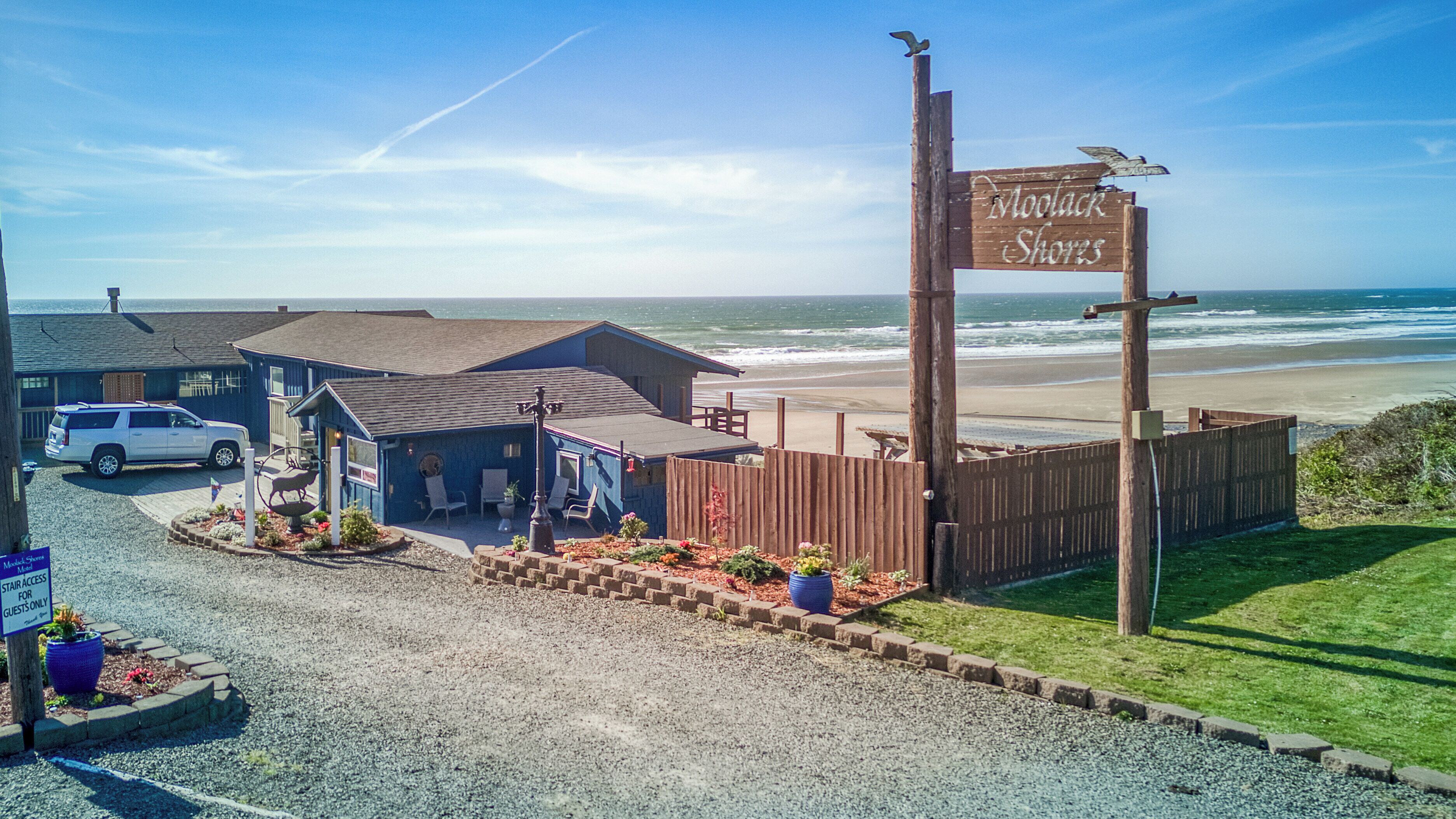 A beachside motel with a sign reading "Moolack Shores" and a parking area with a white SUV.