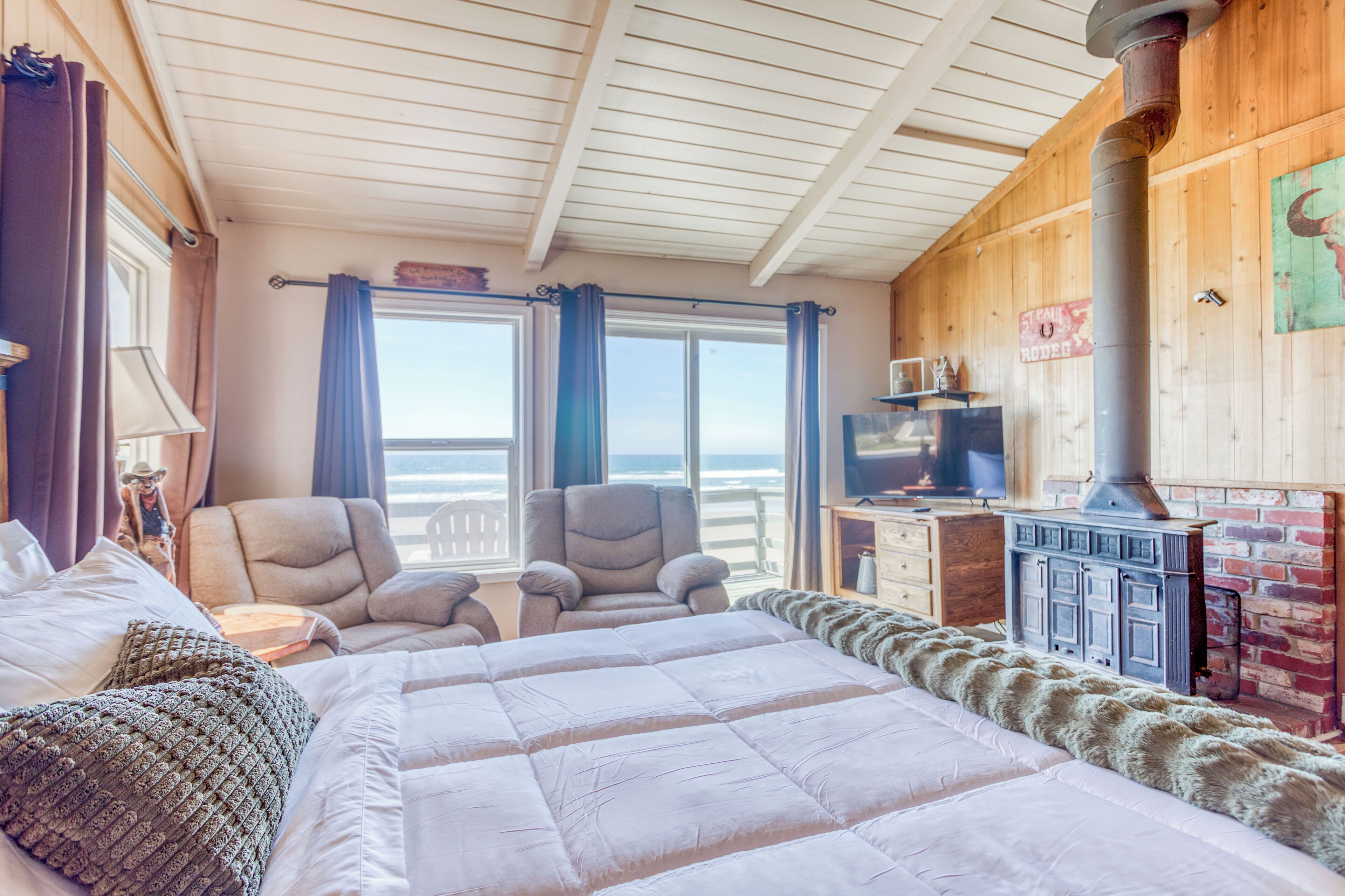 A cozy room with a large bed, two armchairs, a wooden desk, and a fireplace.