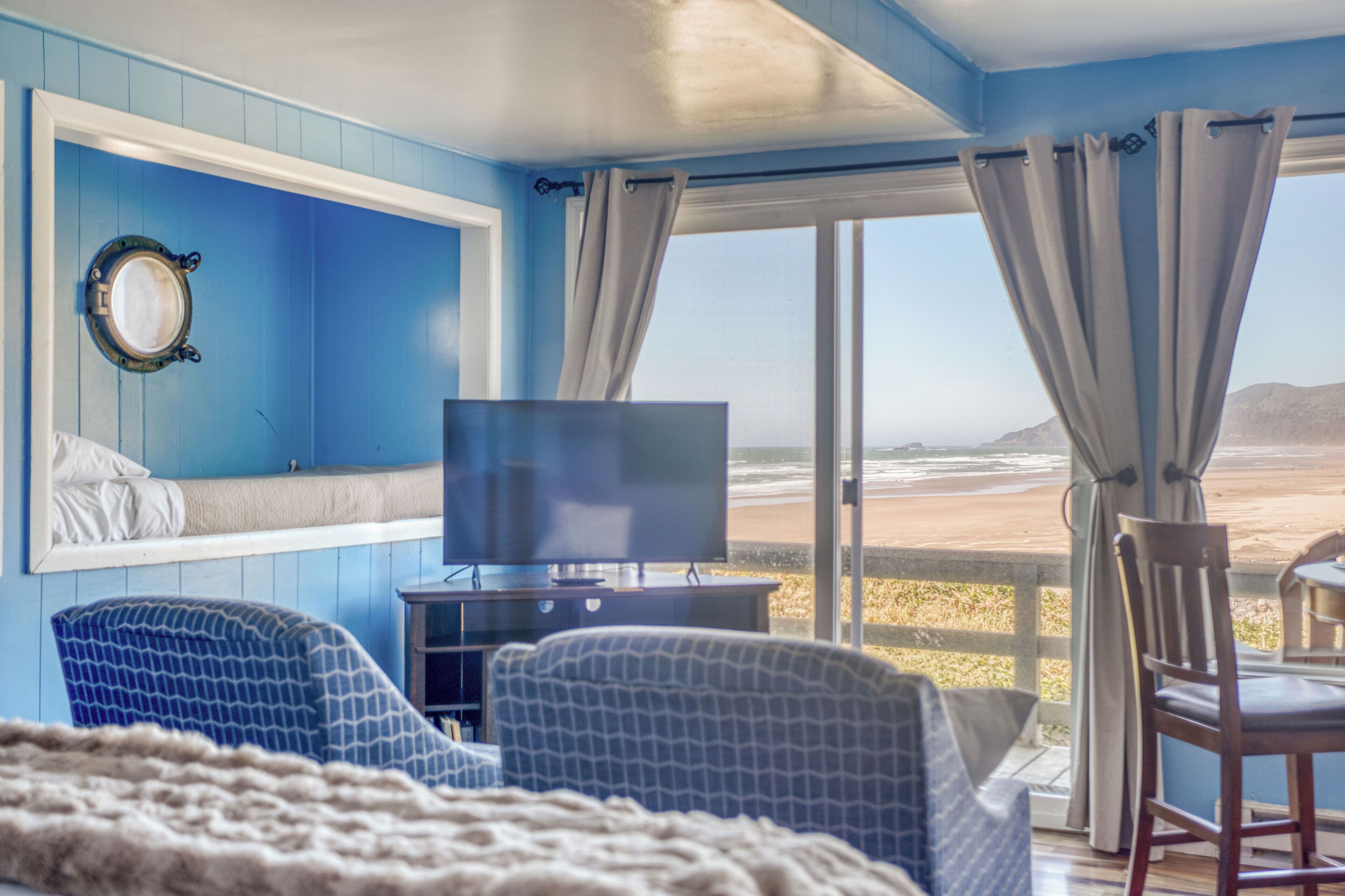 Una habitación con un ventanal amplio, un televisor y dos sillones estampados.