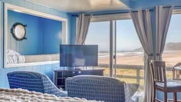 Una habitación con un ventanal amplio, un televisor y dos sillones estampados.