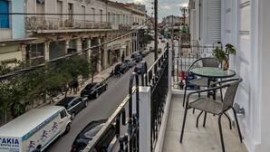 A balcony with a view of a busy street, a table, and chairs. - Casa 1926 (Chania)