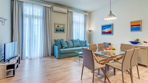 A modern living room with a sofa, TV, dining table, chairs, and artwork. - Casa 1926 (Chania)