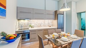 A modern kitchen with grey cabinets, a tiled backsplash, and a dining area with a glass table set for breakfast. - Casa 1926 (Chania)