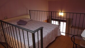 A bedroom with a bed, a window with curtains, a wooden floor, and a metal railing. - Agriturismo Cascina Rossano (Provaglio d'Iseo)