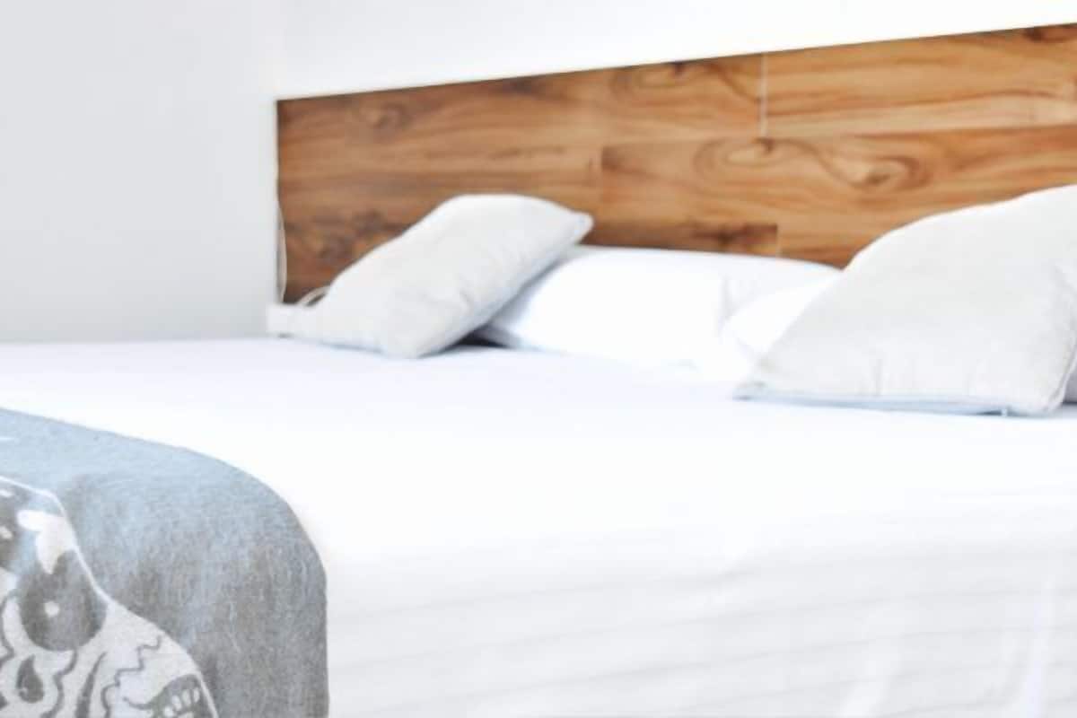A neatly made bed with white linens and pillows, a wooden headboard, and a gray patterned throw blanket.