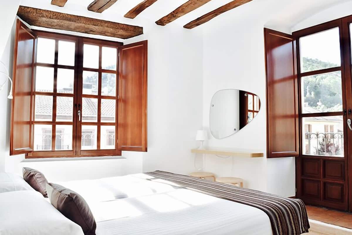 A bedroom with a bed, a bedside table, a mirror, and a window with wooden shutters.