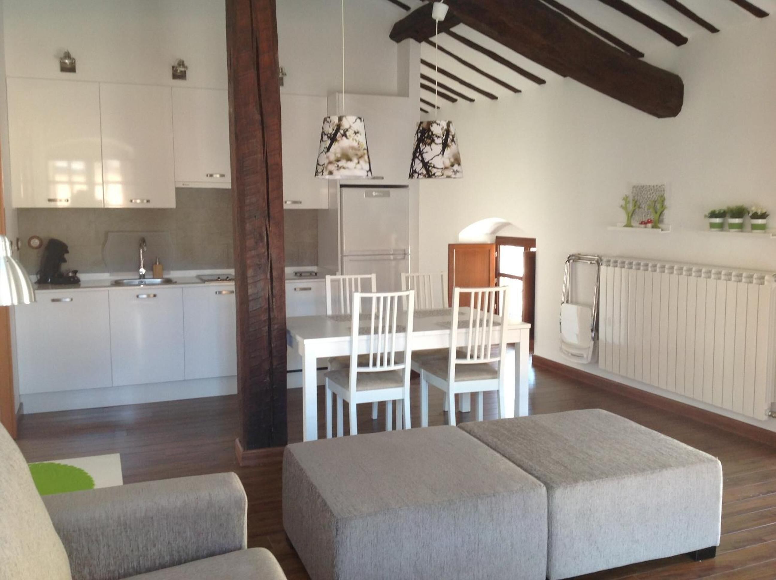 Una cocina moderna con armarios blancos, una mesa de comedor con sillas e iluminación colgante.