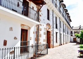 Una estrecha calle adoquinada flanqueada por edificios blancos con detalles de piedra y barandillas de metal negro.