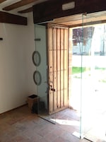 Una puerta de cristal con un panel de madera, un cubo de basura pequeño y un piso de baldosas.