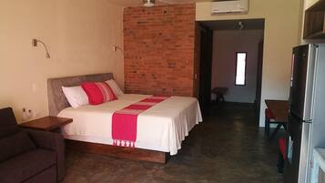 Una habitación de hotel con una cama, ventilador de techo, pared de ladrillo y kitchenette.