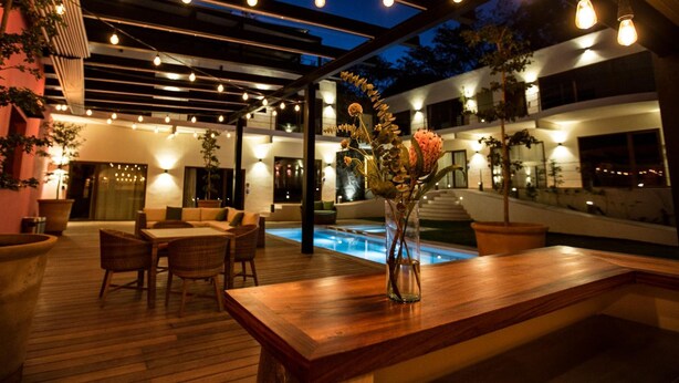 An outdoor patio area with a wooden table, chairs, a vase with flowers, and a pool. - Casa de la Ballena (Sayulita)