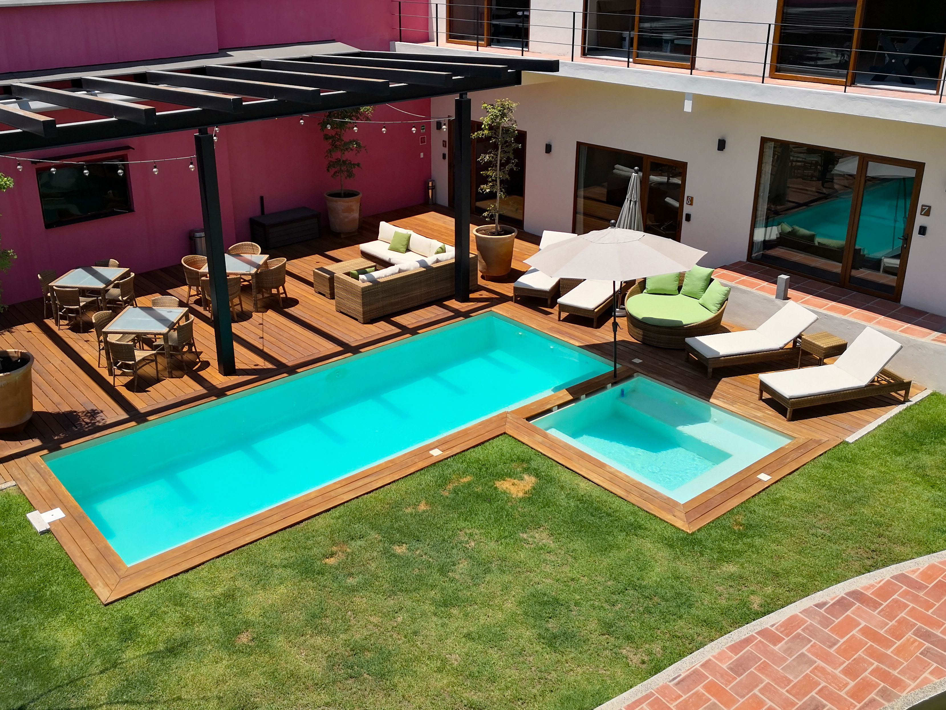 A modern outdoor pool area with wooden decking, lounge chairs, and a pergola.