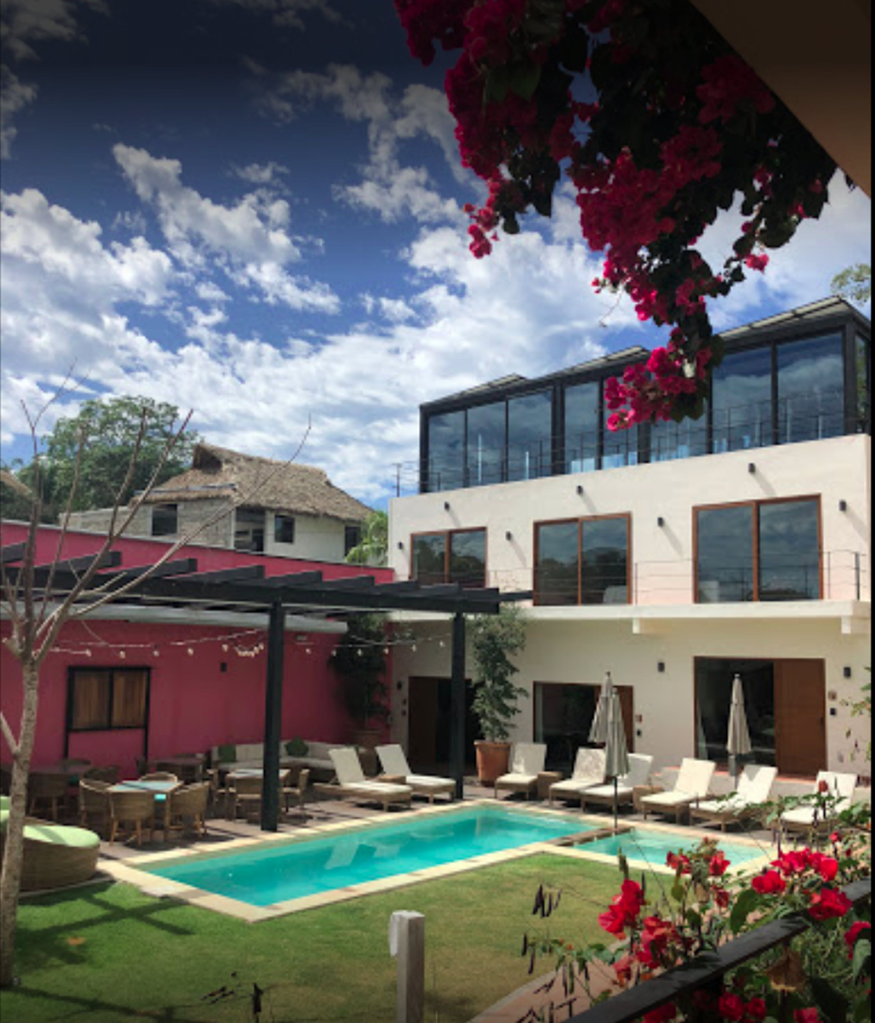 A modern two-story house with a swimming pool, outdoor seating, and a red building in the background.