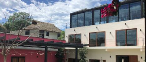 A modern two-story house with a swimming pool, outdoor seating, and a red building in the background.