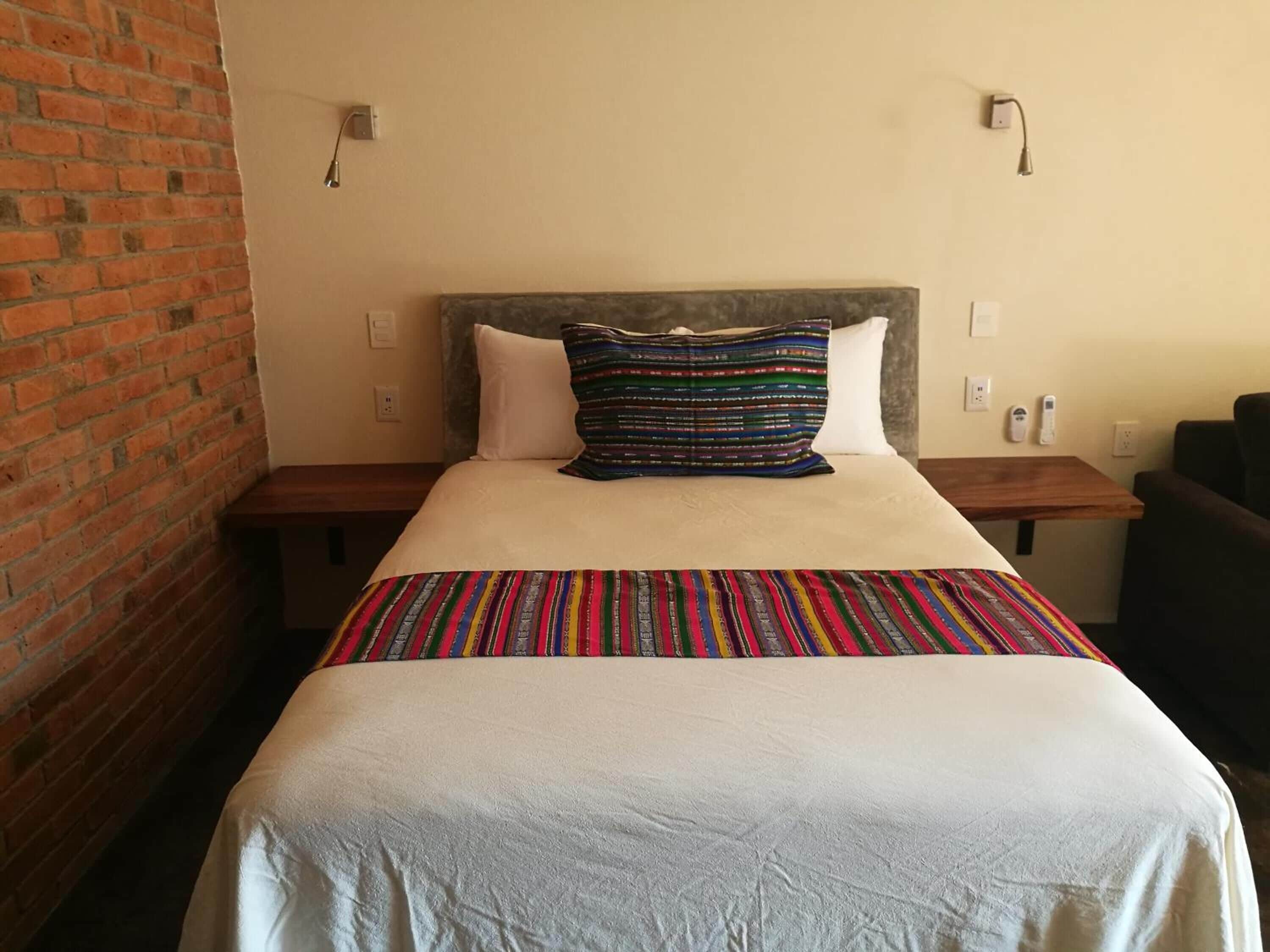 A hotel room with a bed, a brick wall, and a wooden nightstand.