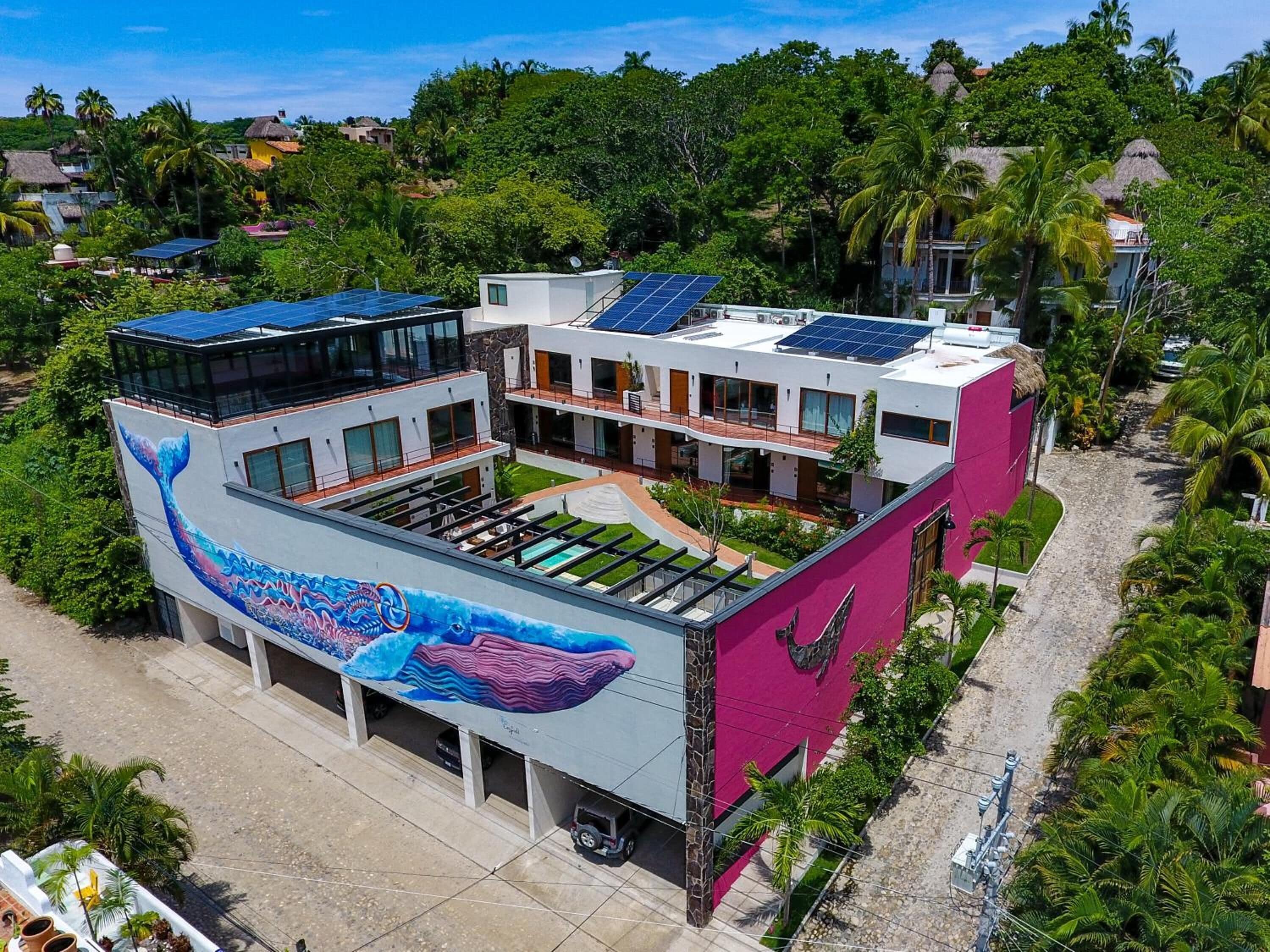 A modern building with a large mural of a whale on the side, solar panels on the roof, and a swimming pool in the courtyard.