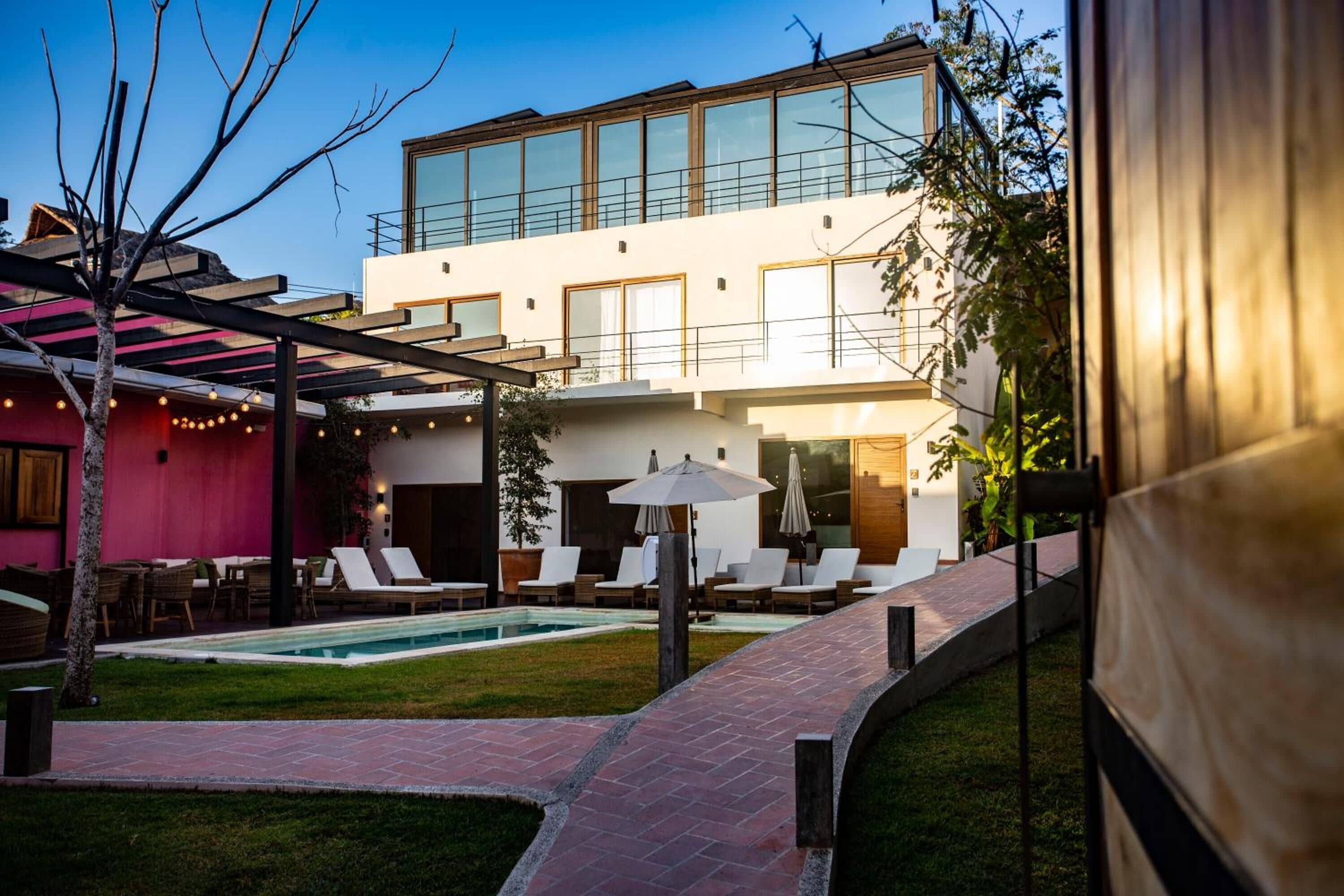 Un edificio moderno con piscina, mobiliario exterior y un patio cubierto.
