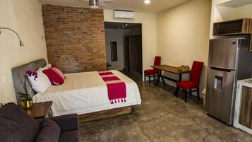 Habitación de hotel con cama, un pequeño espacio para sentarse, refrigerador y pared de ladrillo.