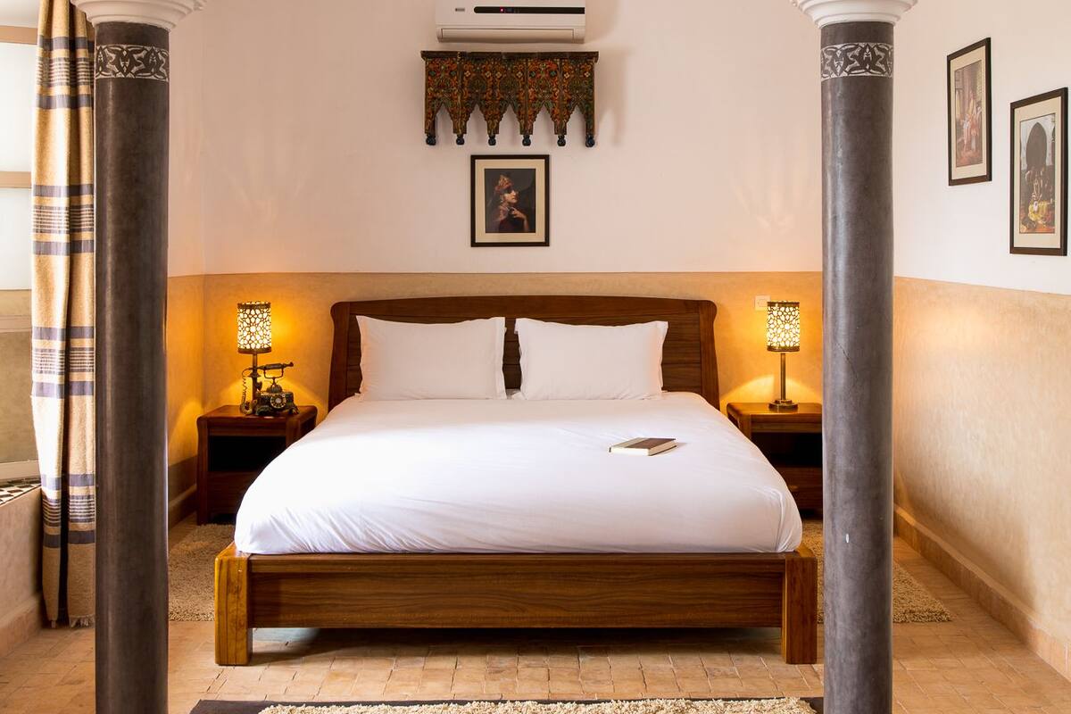Une chambre à coucher avec un grand lit, deux tables de chevet, une lampe suspendue et un élément décoratif mural.