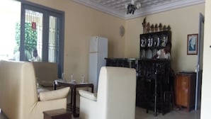 Un salon comprenant un canapé, une petite table, un réfrigérateur et un coin bar avec des bouteilles.
