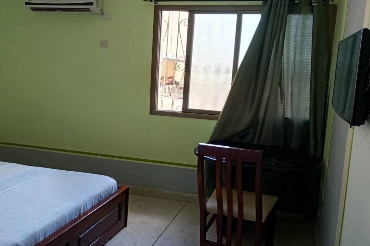 A room with a bed, a chair, a window with curtains, and a wall-mounted air conditioner.