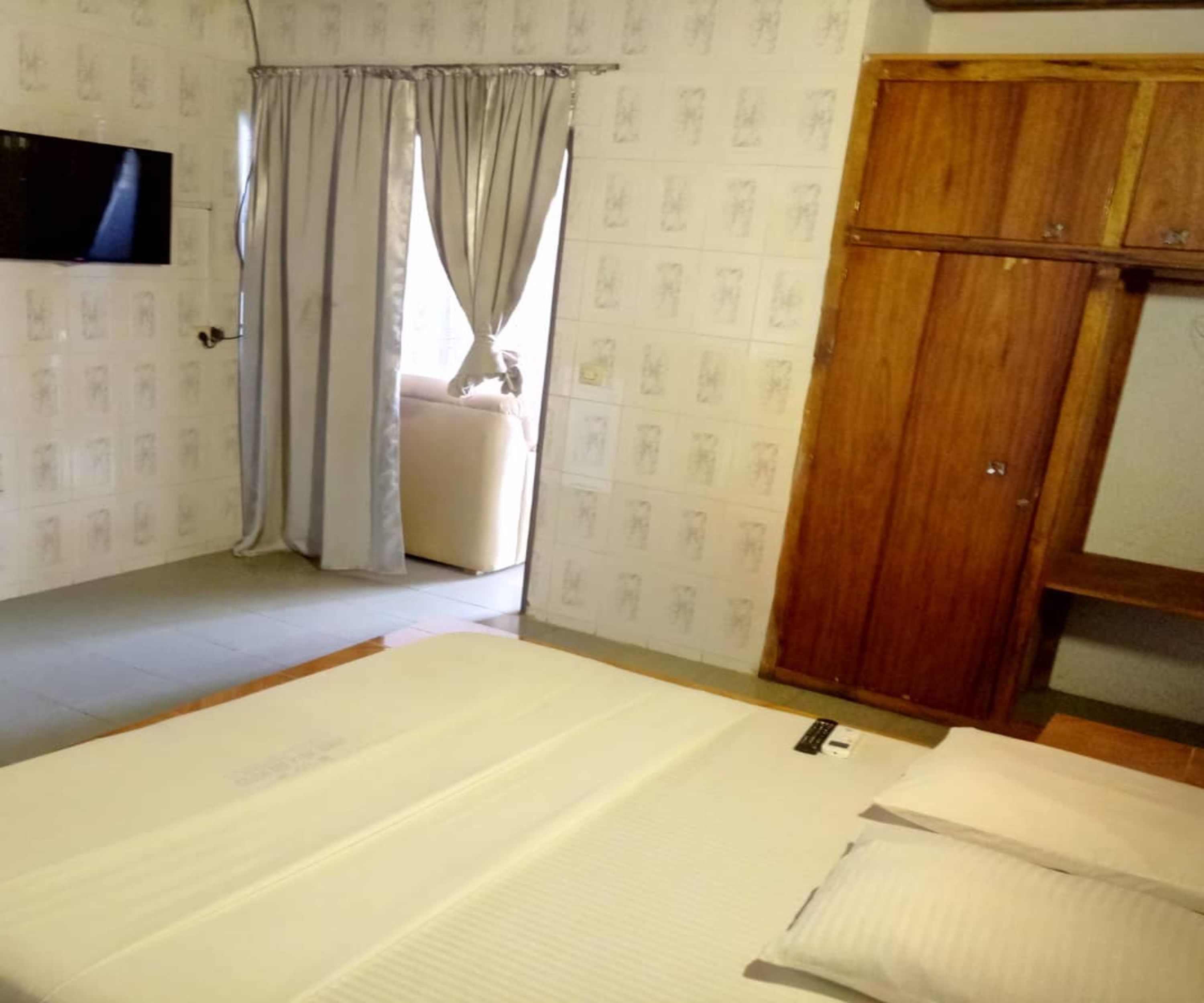 A bedroom with a bed, a wooden wardrobe, and a television on the wall.