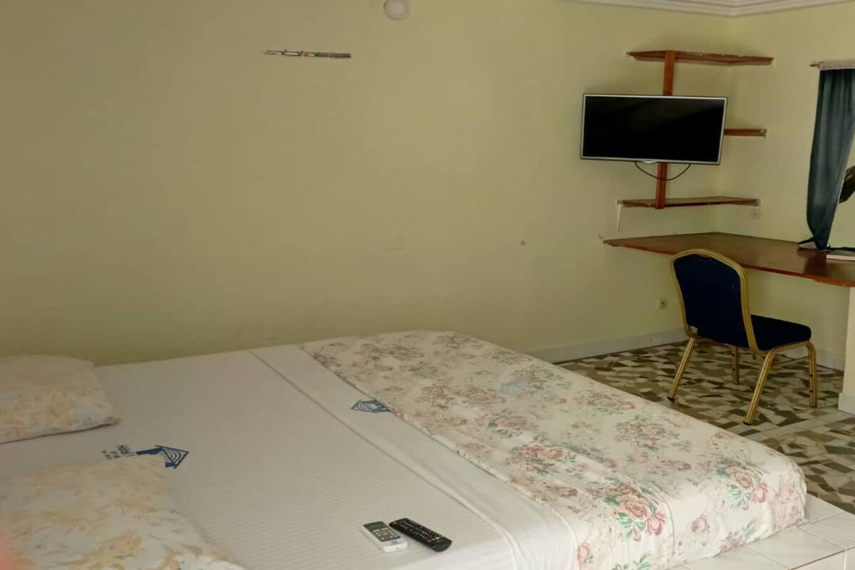 A hotel room with a bed, a desk with a television, and a chair.