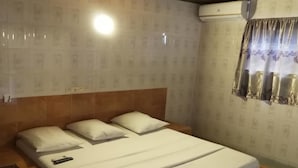 Un lit simple avec une literie et des oreillers blancs, une tête de lit en bois et une table de chevet avec une télécommande.