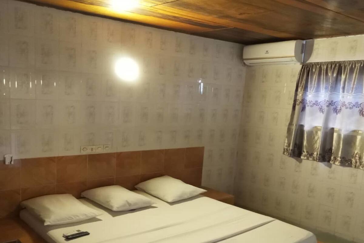 A single bed with white bedding and pillows, a wooden headboard, and a nightstand with a remote control.