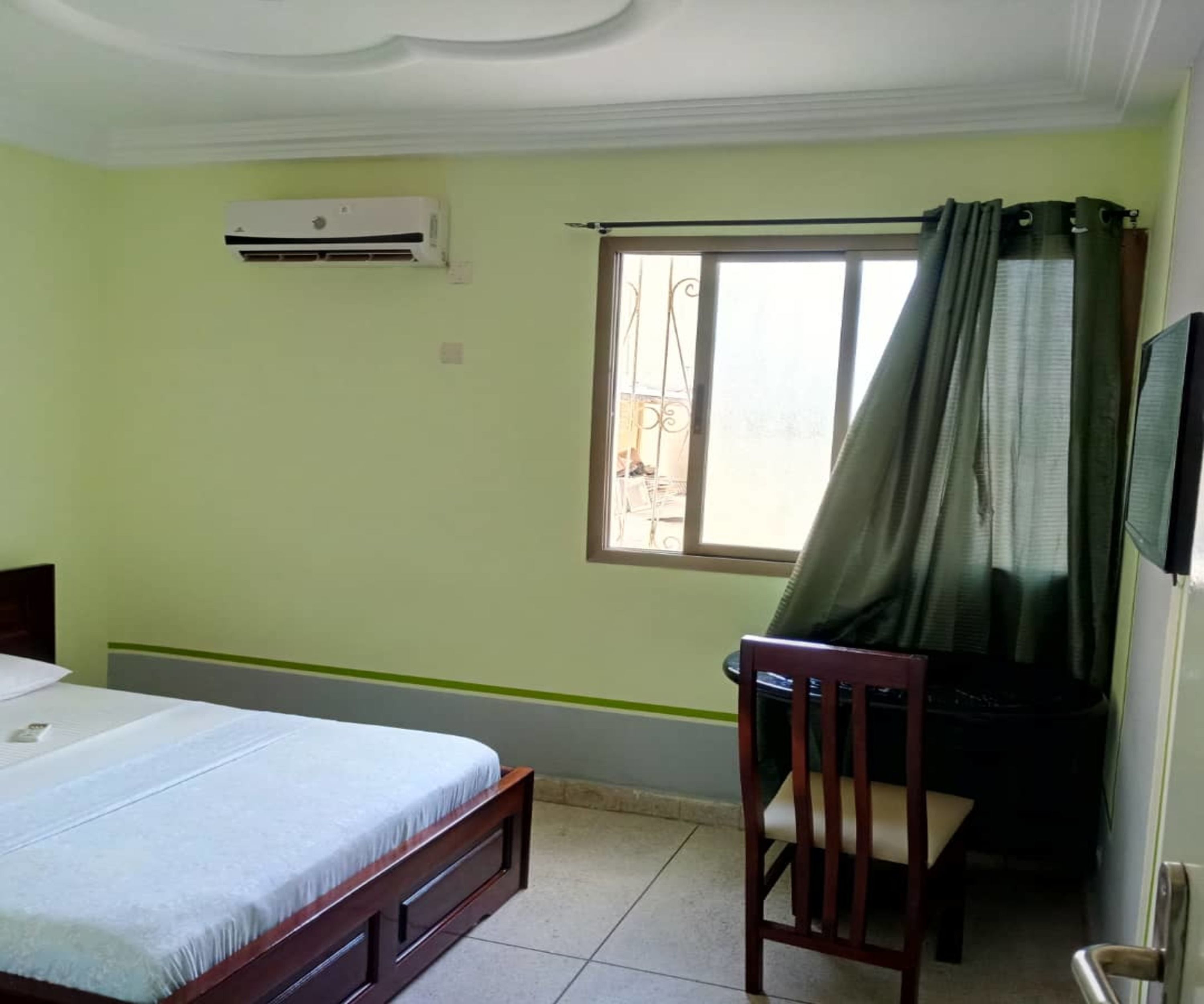A bedroom with a bed, a chair, a desk, and an air conditioning unit.