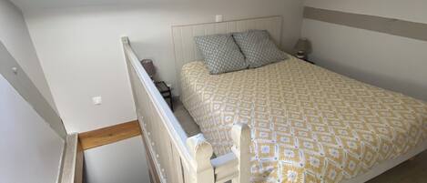 A bedroom with a skylight, a bed with patterned bedding, a nightstand, and a wooden staircase.