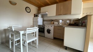 A compact kitchen with white appliances, a dining table with chairs, and a clock on the wall. - Gîte Le Papillon - Le Cocon de Curson (Chanos-Curson)