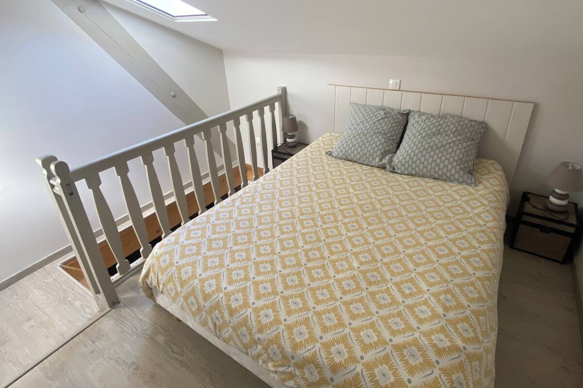 A bedroom with a wooden bed frame, a patterned bedspread, and a sloped ceiling with a skylight.