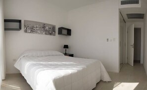 A bedroom with a large bed, a nightstand with a lamp, and two framed pictures on the wall. - The Tower (Asunción)