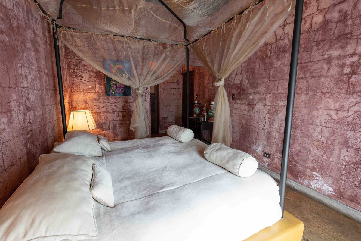 Ein Bett mit Baldachin, eine Lampe und eine Wand mit strukturierter Oberfläche.