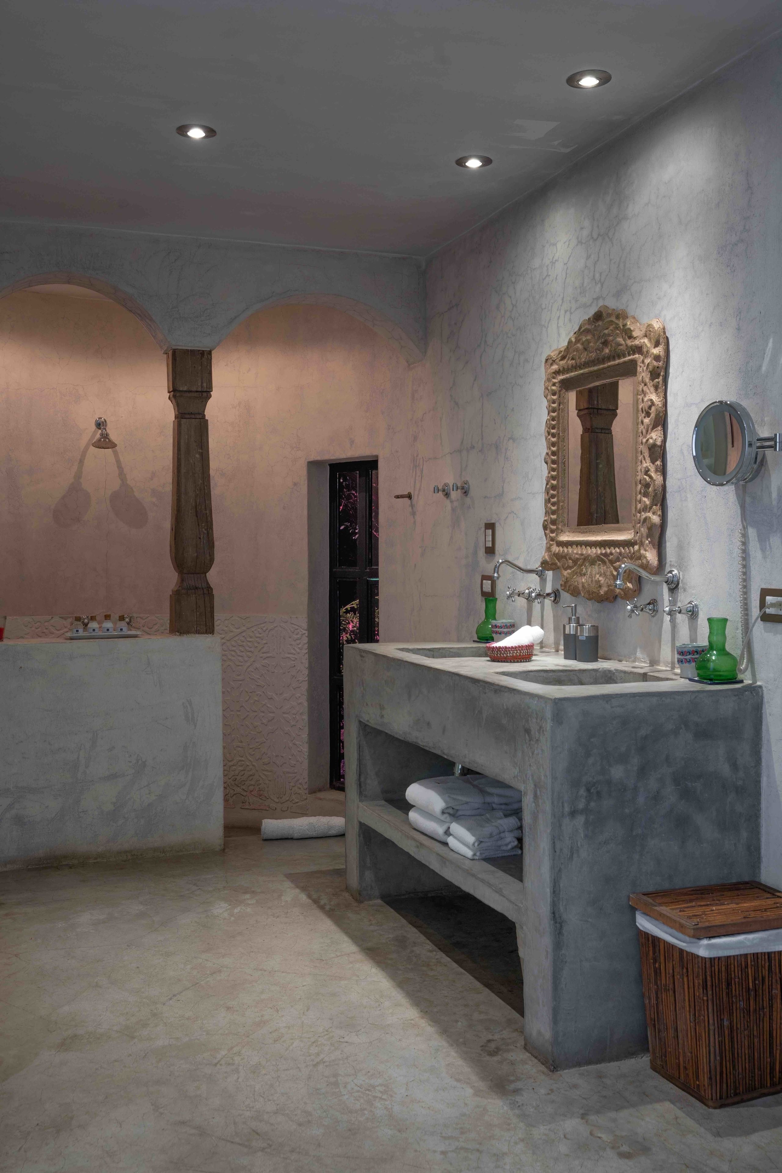 Un baño con un lavamanos grande de mármol, un espejo y un pilar de madera.